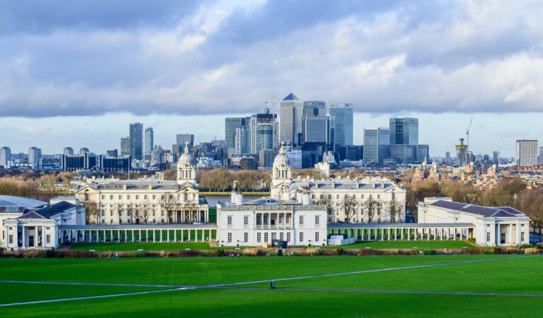 Panoramic view of Greenwich Park with London skyline featuring iconic buildings and lush lawns.