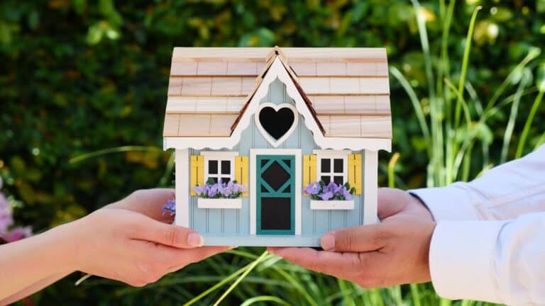 Close-up of hands holding a detailed miniature house model, symbolizing goals of homeownership and noise surveys for small developments.