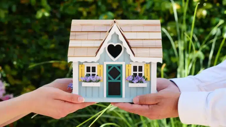 Close-up of hands holding a detailed miniature house model, symbolizing goals of homeownership and noise surveys for small developments.