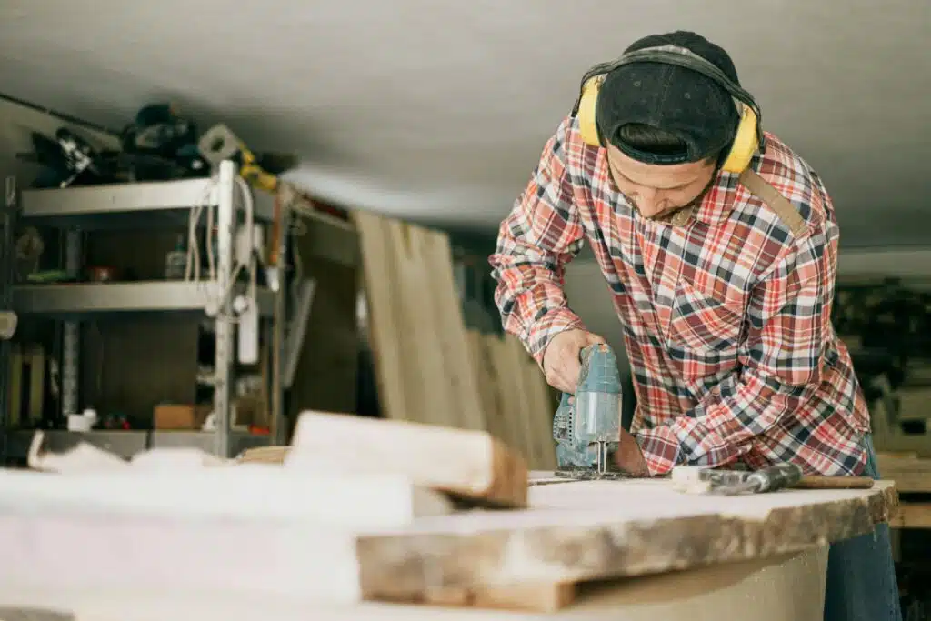 A skilled carpenter uses a power drill in a well-organized woodworking workshop. The Control of Noise at Work Regulations 2005