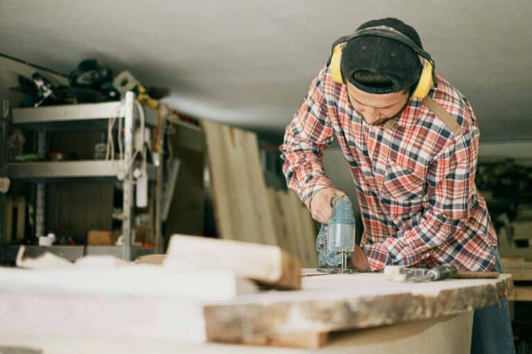 A skilled carpenter uses a power drill in a well-organized woodworking workshop. The Control of Noise at Work Regulations 2005