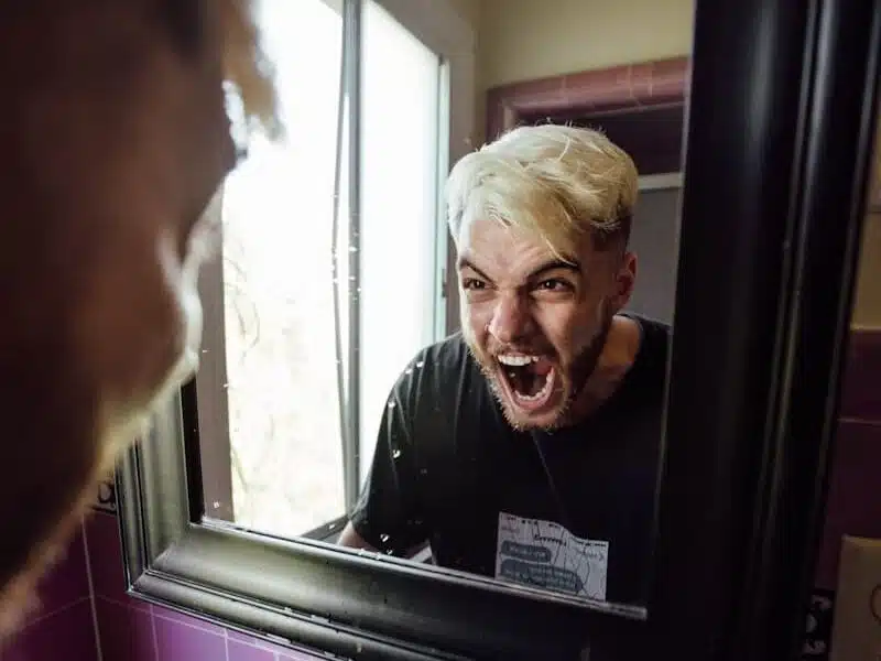 man in black crew neck shirt, screaming at the mirror because he needs to submit a noise complaint and deal with noise nuisance.