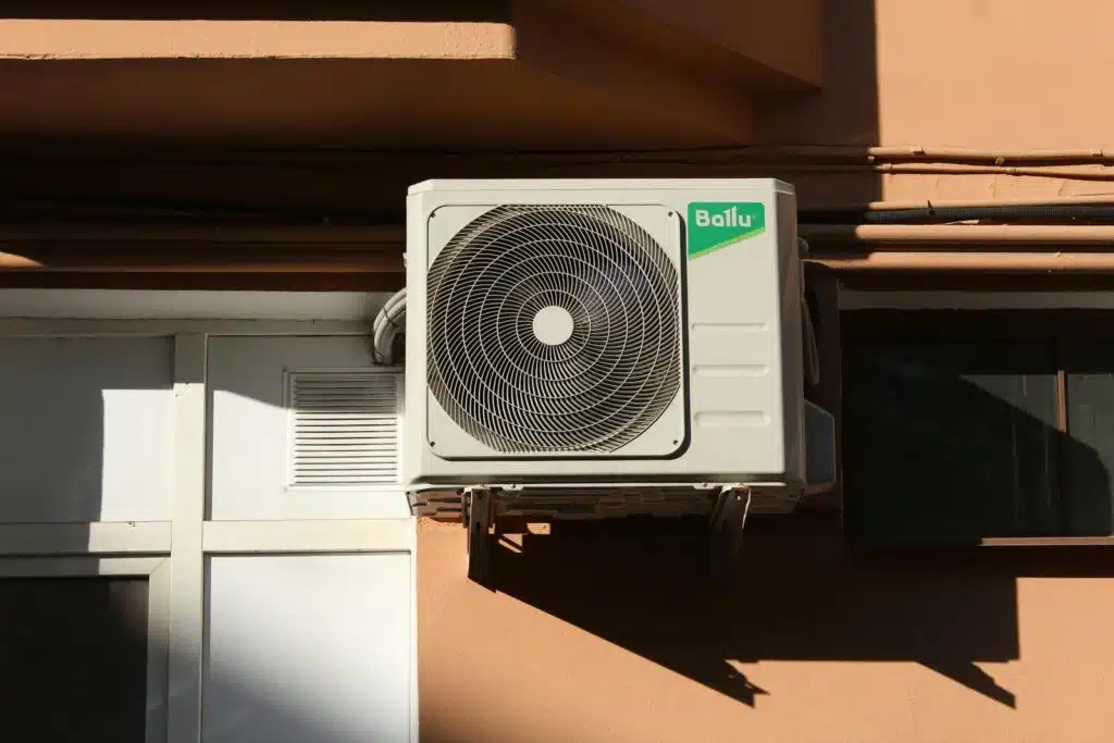 A Ballu air conditioner condenser unit mounted on a building exterior, showcasing modern HVAC technology. Noisy heat pump. Air source heat pump noise complaints and mitigation.