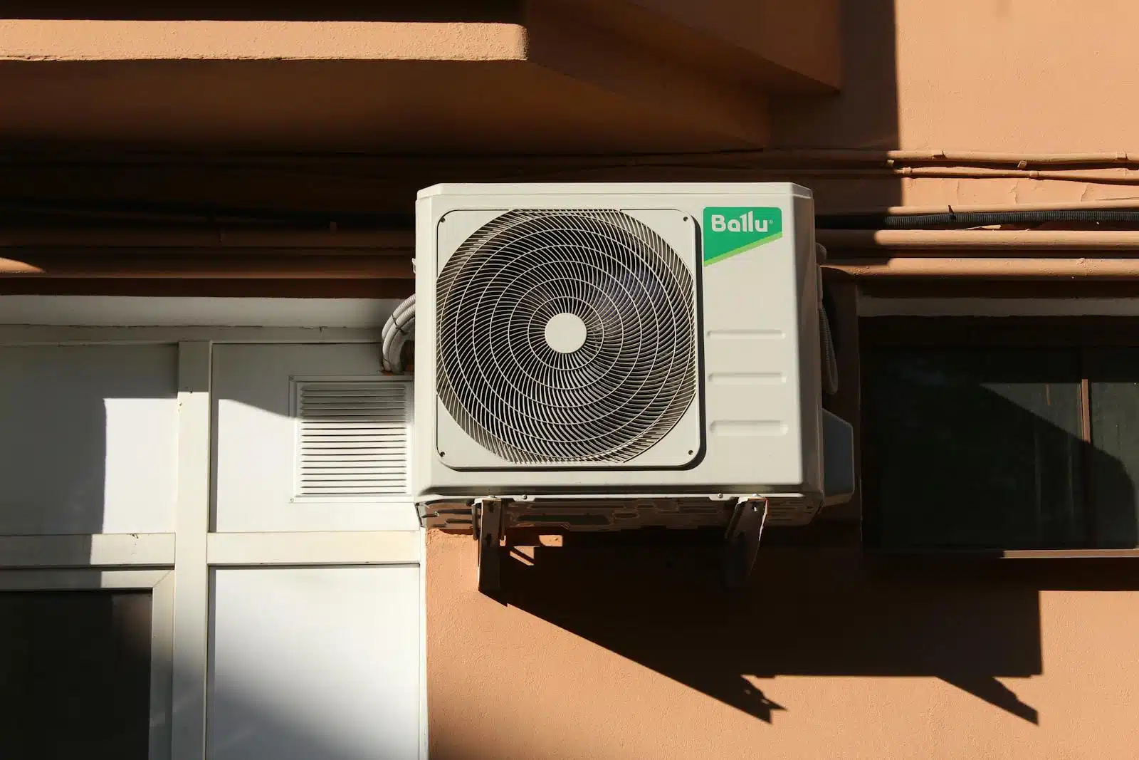 Photo by Gustav Mahler A Ballu air conditioner condenser unit mounted on a building exterior, showcasing modern HVAC technology. Noisy heat pump. Air source heat pump noise complaints and mitigation.