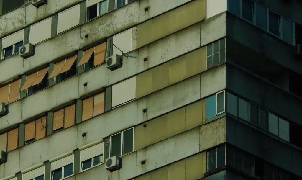 Close-up of a weathered residential building facade with air conditioning units and varied window styles ashp.