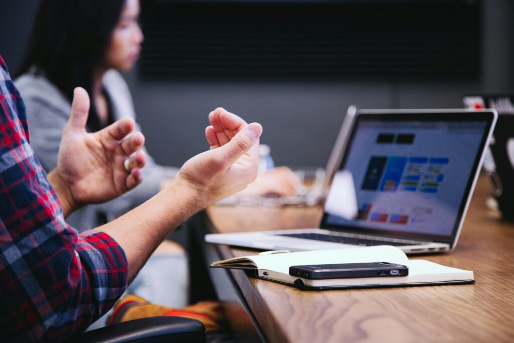 person gesturing during meeting with laptop about FAQs for noise impact assessment for planning Noise impact assessment report structure for UK planning applications