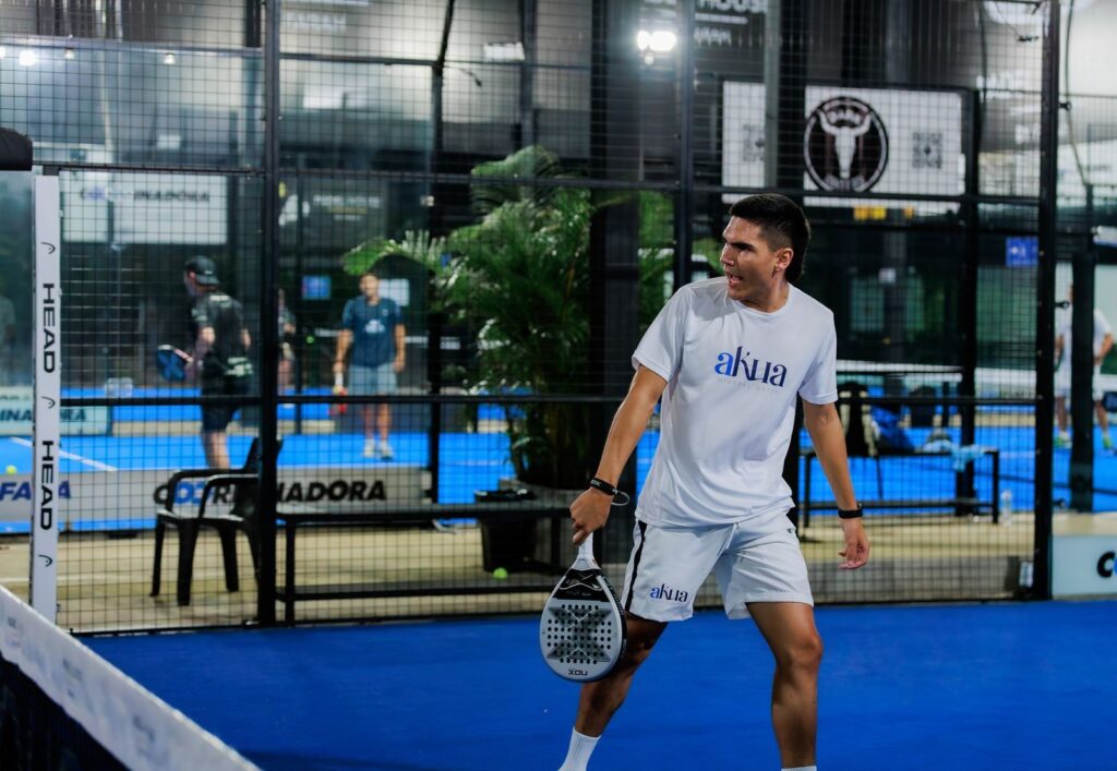 Energetic padel tennis player at indoor court mid-match for padel court planning application.